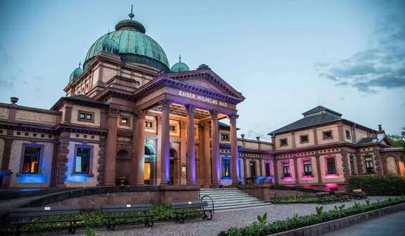 Vergrößerte Ansicht: Frontansicht Kaiser-Wilhelms-Bad bei Nacht, farbig beleuchtet