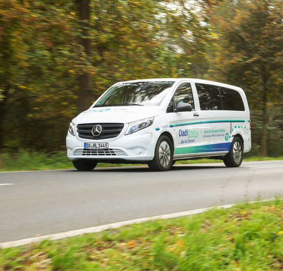 DadiLiner Ein weißes großes Auto fährt auf einer Straße im Grünen