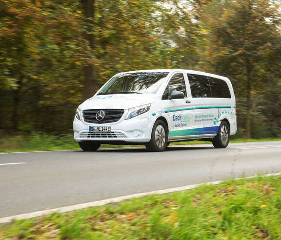 DadiLiner Ein weißes großes Auto fährt auf einer Straße im Grünen