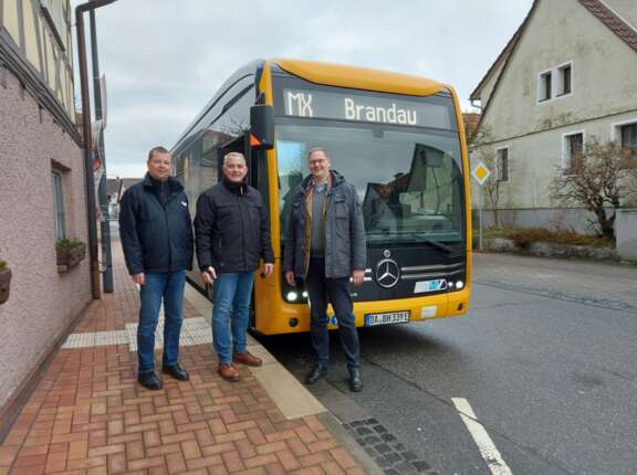 Drei Männer stehen auf dem Bürgersteig vor einem gelben Bus