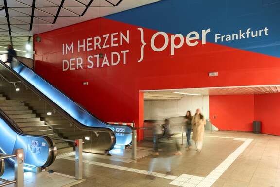 Eine Rolltreppe, rot-blaue Wände, Schrift: Im Herzen der Stadt Oper Frankfurt
