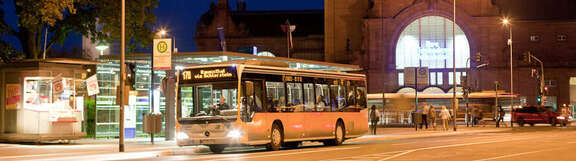 Vergrößerte Ansicht: Bus in der Dunkelheit an einer Haltestelle vor einem Bahnhofsgebäude