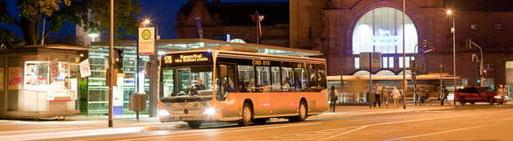 Bus in the dark stopping at a bus stop in front of a station building