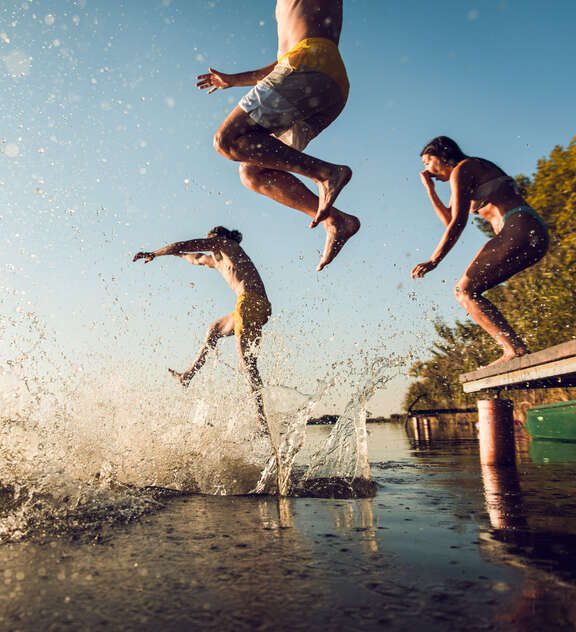 Drei Menschen springen vom Steg in einen Badesee