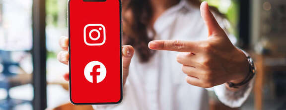 Frau zeigt auf ein Smartphone mit rotem Bildschirm, auf dem die Symbole von Instagram und Facebook zu sehen sind.