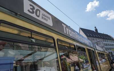 Ein Zug mit der Aufschrift Tramrestaurant fährt quer durchs Bild, oben blauer Himmel mit einzelnen Wolken