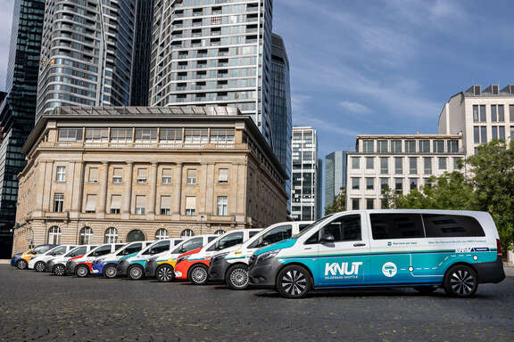 Autos stehen seitlich in einer Reihe leicht versetzt auf einem Platz vor einem historischen Gebäude. Im Hintergrund Hochhaus
