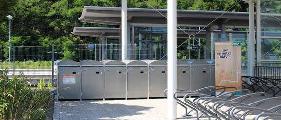 Acht Fahrradboxen an einer RMV-Bahnstation, davor sind weitere Fahrradständer installiert