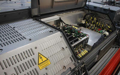 Zwei graue Kästen. Links ein Warnschild mit einem Blitz und darunter die Aufschrift "Hochspannung Lebensgefahr" Daneben ist der Kasten geöffnet mit vielen Kabeln und Drähten