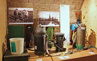 Vergrößerte Ansicht: alte Kanister und zwei alte Fotos in Museumsausstellung