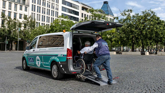 Ein Mann schiebt einen Rollstuhlfahrer in den Kofferraum eines Vans.