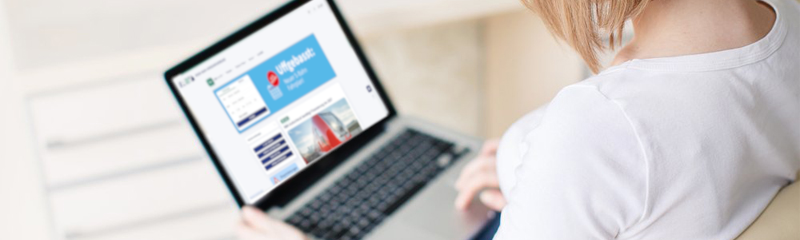 Eine Frau sitzt mit einem Laptop auf dem Schoß in einem beigen Sessel. Man sieht die Webseite RMV aktuell