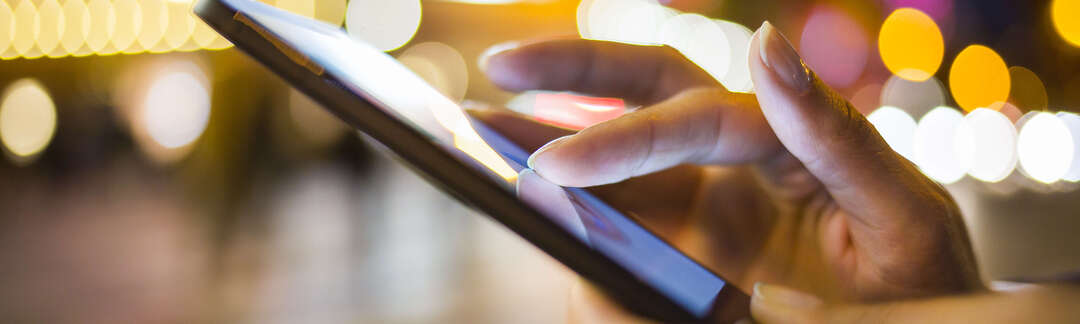 Hände die ein Smartphone bedienen draußen bei Nacht