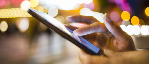 Hände die ein Smartphone bedienen draußen bei Nacht