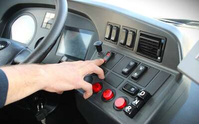 Eine Hand betätigt eine Taste in einer Busfahrer-Kabine