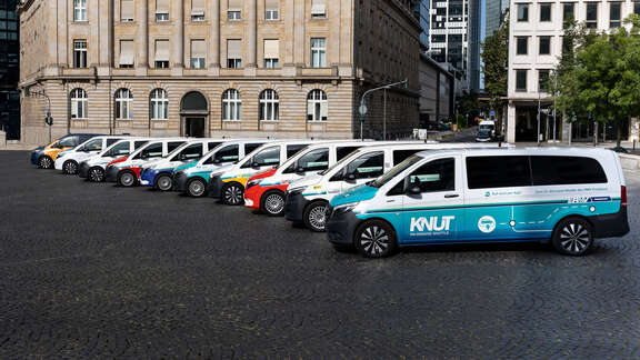Verschiedene Fahrzeuge stehen in einer Reihe versetzt vor einem Gebäude. Seitliche Sicht auf die Fahrzeugflotte