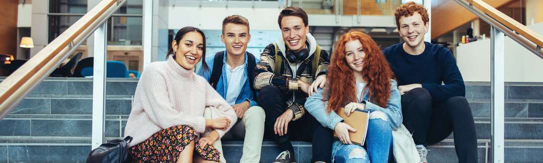 Fünf Schülerinnen und Schüler sitzen in einem Gebäude auf Treppenstufen 