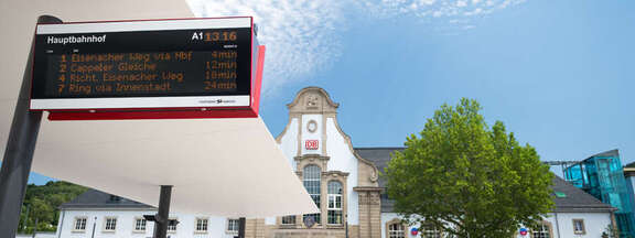 digitale Anzeigetafel am Bahnhofs-Vorplatz, im Hintergrund das Bahnhofs-Gebäude