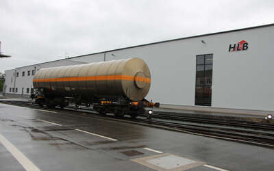 Im Hintergrund ein großes graues Gebäude mit dem HLB Logo, vorne ein Transportfahrzeug auf Gleisen.