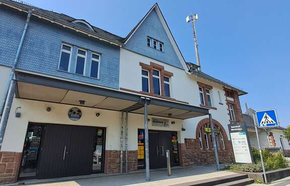 Ein altes Gebäude mit einem Aufsteller davor, Schrift: Bahnhof Mörfelden