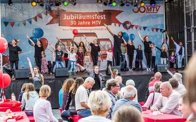 Kinder und Jugendliche performen Streetdance auf der Jubiläumsbühne. Davor sind Tische mit Zuschauern. 