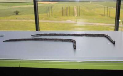 Vergrößerte Ansicht: Sensen in einer Ausstellungsvitrine vor dem Panoramafenster