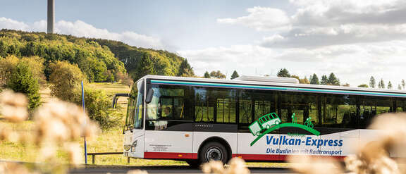 Bus des Vulkan-Express vor der Silhouette des Fernsehturmes auf dem Hoherodskopf
