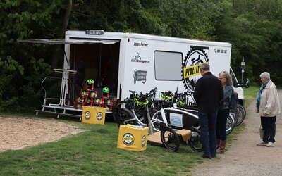 Eine Menschengruppe schaut sich die E-Bikes des Pedelity-Standes an. Im Hintergrund steht ein Transporter von Pedelity mit Fahrradhelmen. 