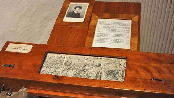 Brüder Grimm-Haus Reisetagebuch Vergrößerte Ansicht: Holztisch mit Abroll-Mechanismus, darauf schwarz-weiß Zeichnungen