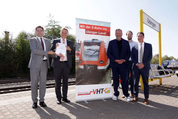 4 Männer zwei links zwei rechts, daneben ein Banner auf einem Bahnsteig in Usingen